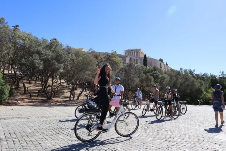 Group of riders and an enthusiastic girl standing on eBike under Acropolis hill