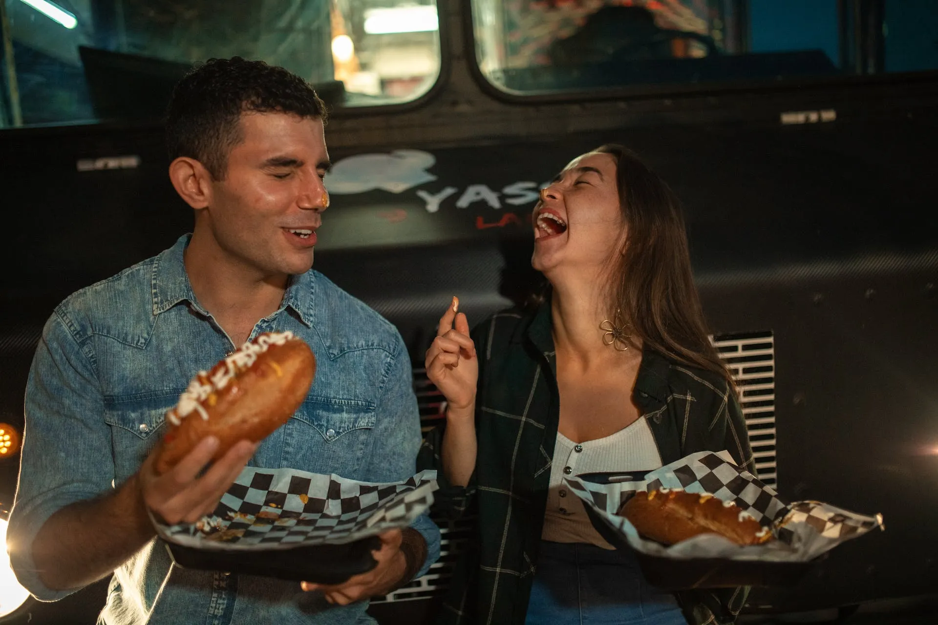 a couple laughs and enjoys street food in front of van