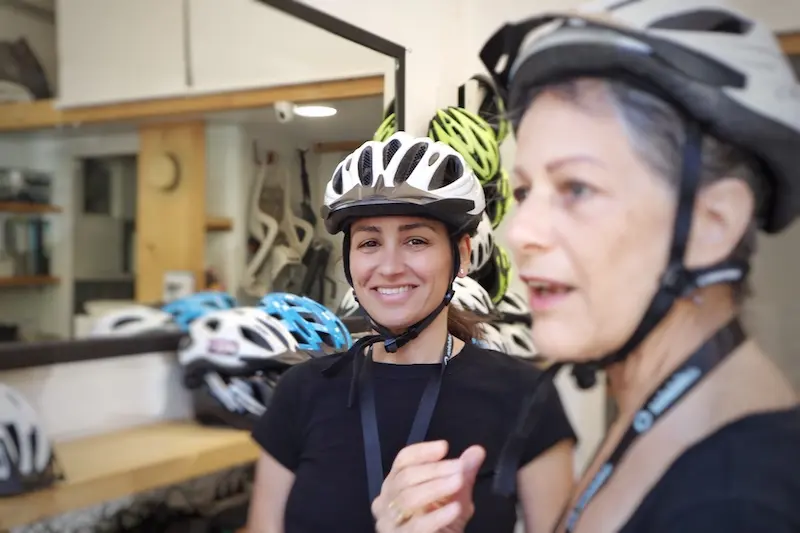 Two female travelers getting fitted with helmets and e-bike gear at the Solebike tour office in Athens.