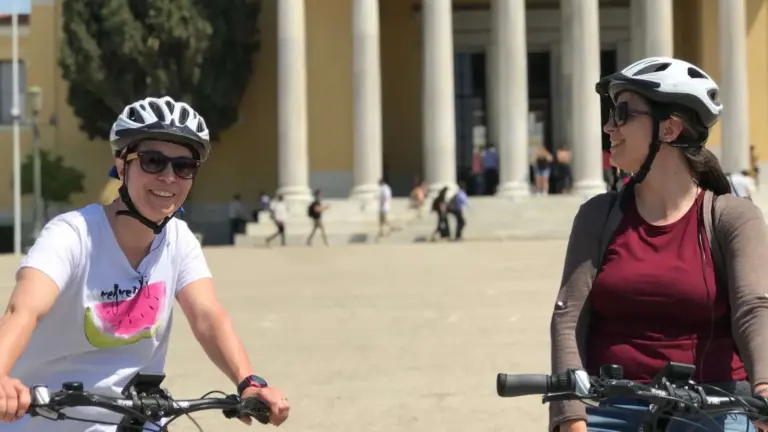 Two riders on a bike tour near a neoclassical building in Athens