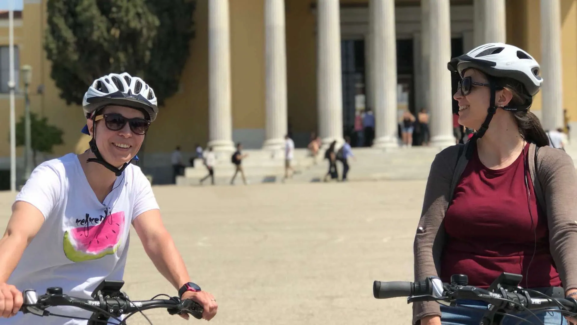 Two riders on a bike tour near a neoclassical building in Athens