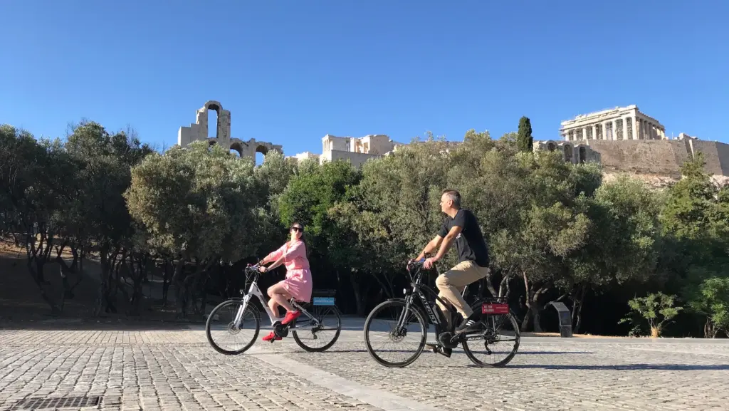 Two riders on eBikes along Dionysiou Areopagitou with the Acropolis in the background