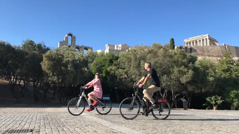 Two riders on eBikes along Dionysiou Areopagitou with the Acropolis in the background