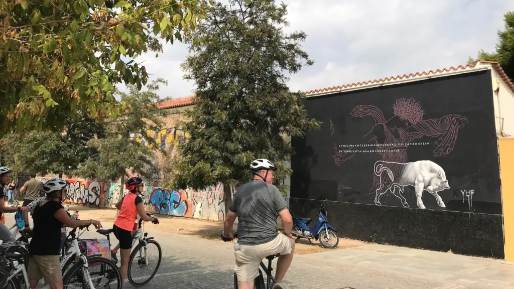 Bike tour group riding through Keramikos beside a large street art mural in Athens