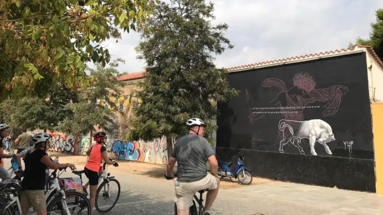 Bike tour group riding through Keramikos beside a large street art mural in Athens