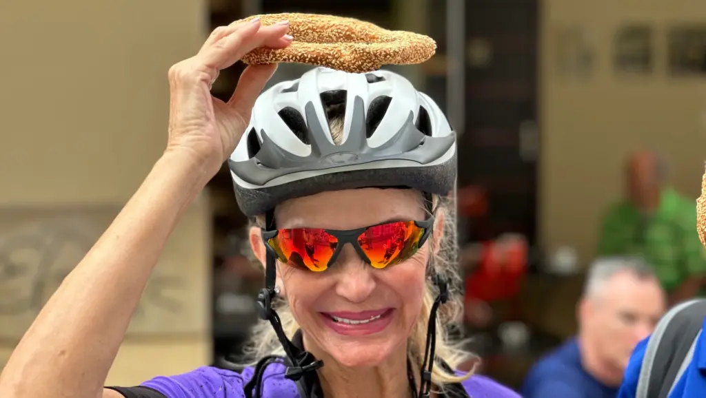 Woman wearing a bike helmet holding a koulouri during a street food stop in Psiri, Athens