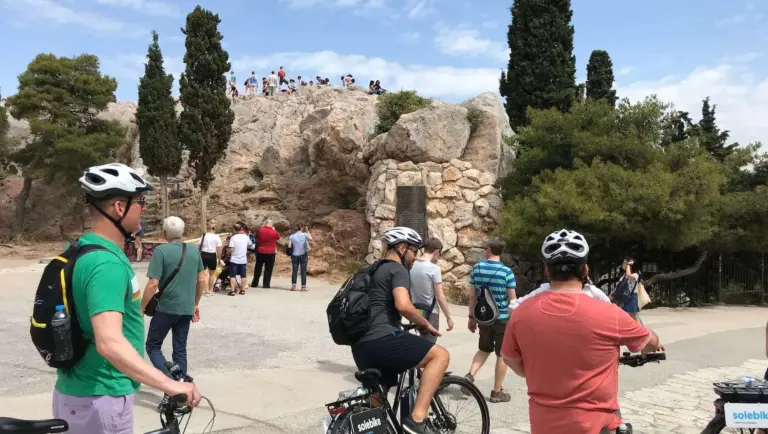 eBike riders stopping below Areopagus Hill in Athens, with visitors standing on the rocky summit