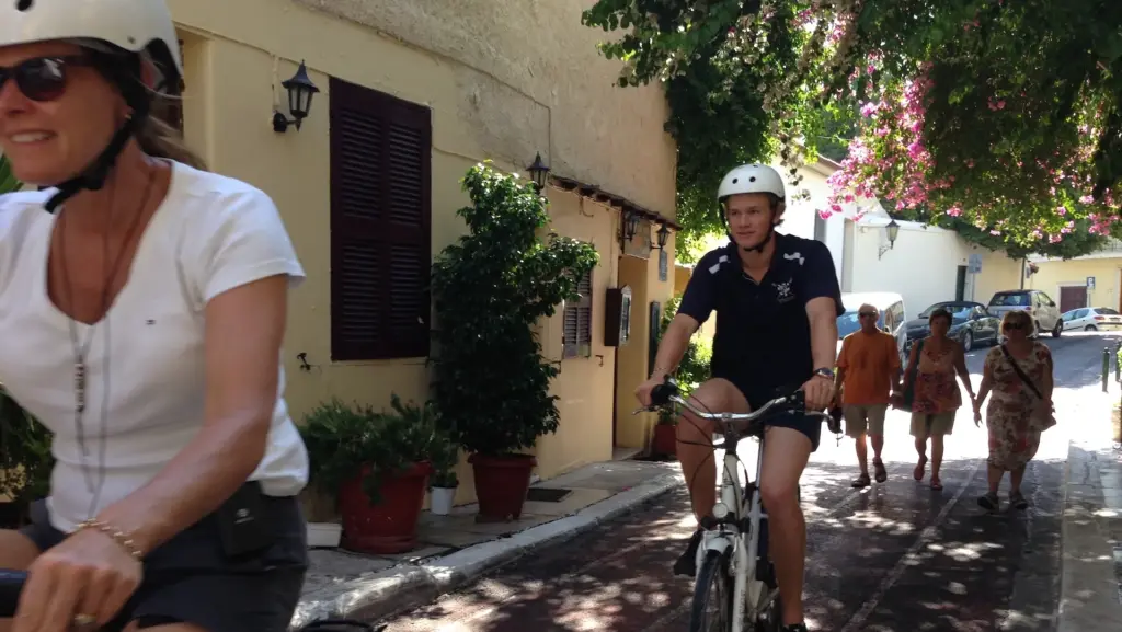 Cyclists riding along Lysiou Street in Plaka, Athens, beneath bougainvillea and old houses