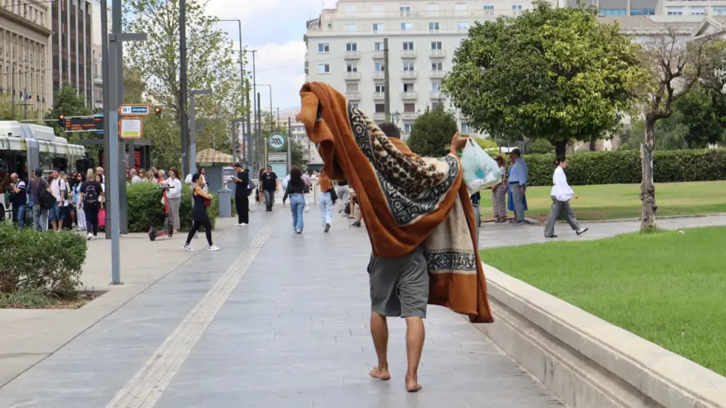 A symbolic street moment in Athens with a blanket-covered figure evoking modern Diogenes