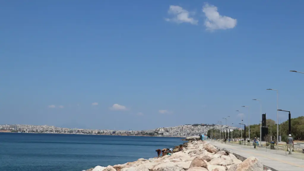 View toward Piraeus from Faliro promenade during the Athens Riviera Coffee Ride, with the seafront path, rocky shoreline, and calm blue water