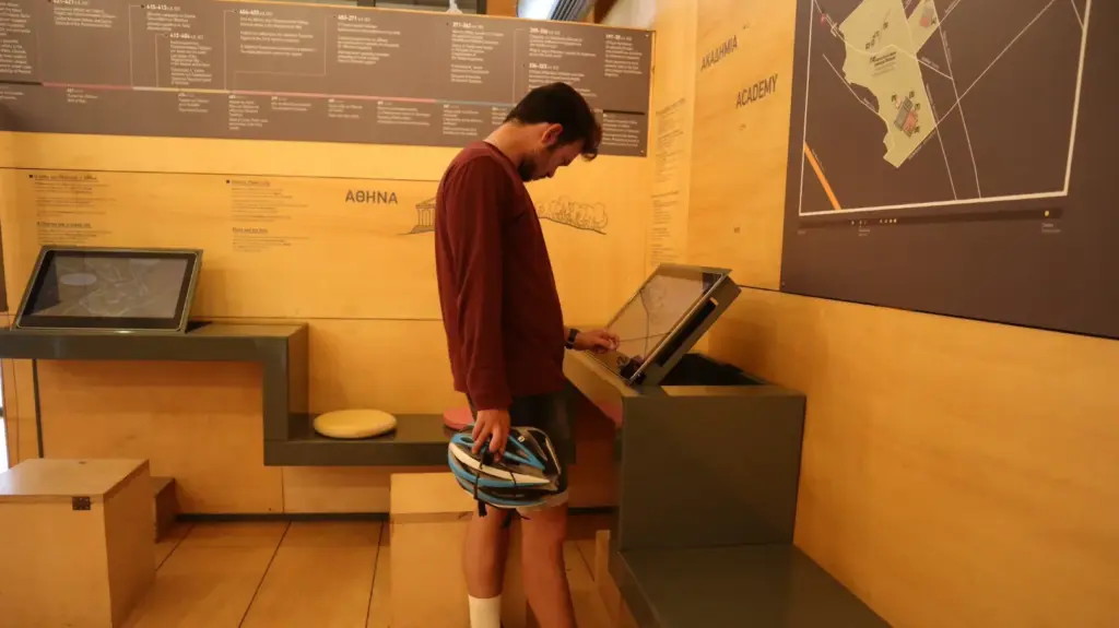 Visitor with bike helmet using a touchscreen exhibit at Plato’s Academy Museum in Athens
